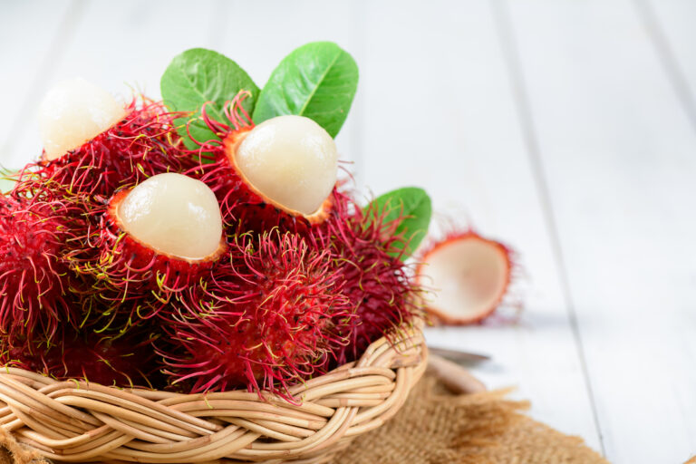 Fresh Rambutan fruits with leaves on bamboo basket on wood backg